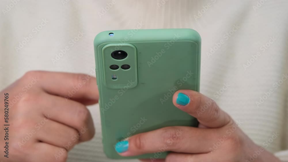 Close-up of female hands holding smartphone. Relaxed young woman in white sweater looking at mobile phone screen enjoying using mobile app for shopping, enjoy playing games at home. Close-up of female hands holding smartphone. Relaxed young woman in white sweater looking at mobile phone screen enjoying using mobile app for shopping, enjoy playing games at home.