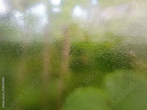 Foggy window glass with raindrops and green nature background