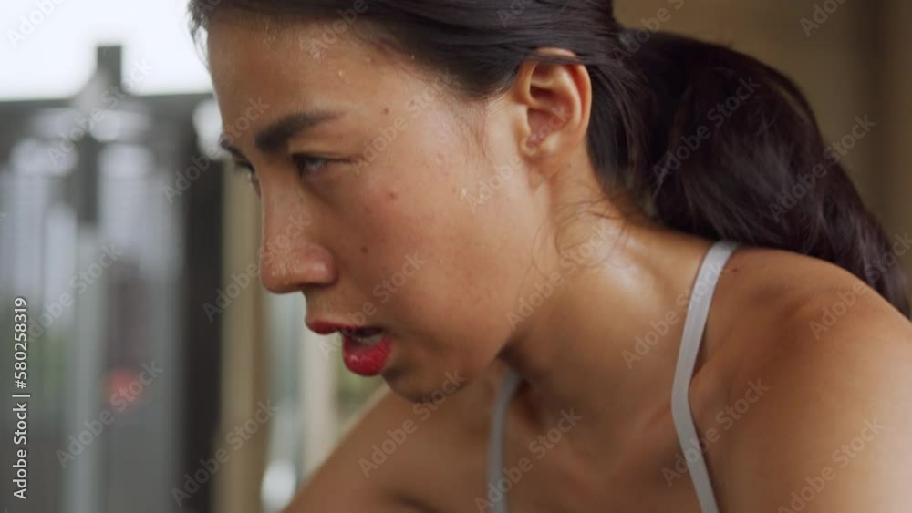 Close-up young Asian female sweat fitness sport woman wear sports bra focus face concentrate with biking keep pedal cycling on bike tech gear cardio endurance in gym. Exercise for good health concept.