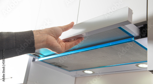Male hand using cooker hood in modern kitchen.