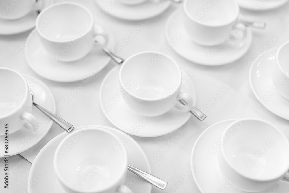 Fototapeta premium Many rows of white ceramic coffee or tea cups. Lines of coffee cups in front of conference room. White ceramic cups and saucers laid out on a buffet table at a catered event for serving a hot beverage