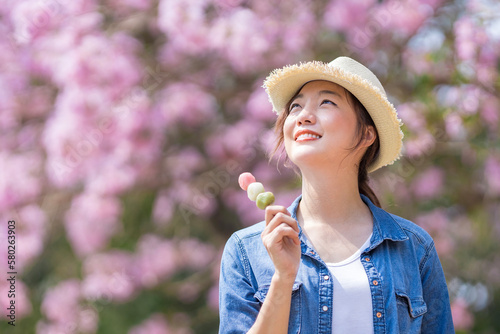 Asian woman holding the sweet hanami dango dessert while walking in the park at cherry blossom tree during spring sakura festival with copy space