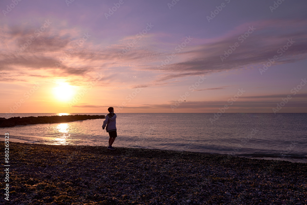 Boy playing pebble throwing on the beach at dawn