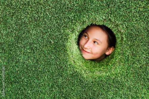 Artificial turf green background. Little kid looks into round hole in a wall made of synthetic turf grass. Eco concept. Place for text. photo
