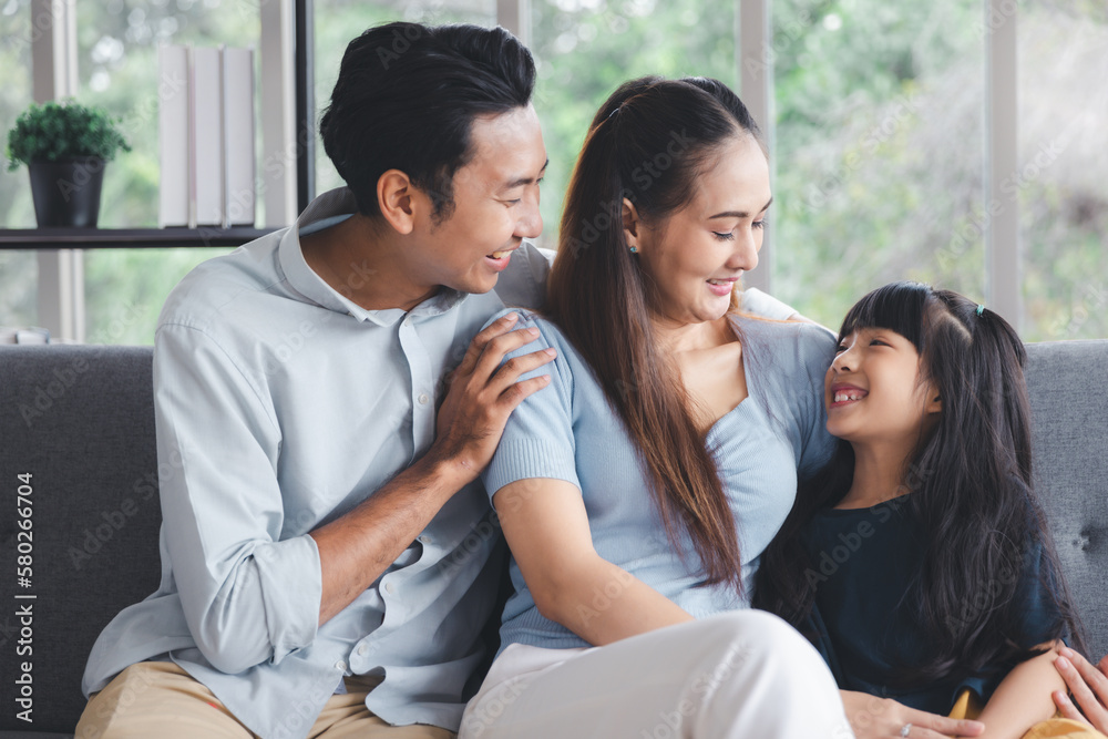 Cheerful young family father mother and daughter smiling embrace sitting on couch in living room at home, Family quality time concept Cheerful young family father mother and daughter smiling embrace sitting on couch in living room at home, Family quality time concept