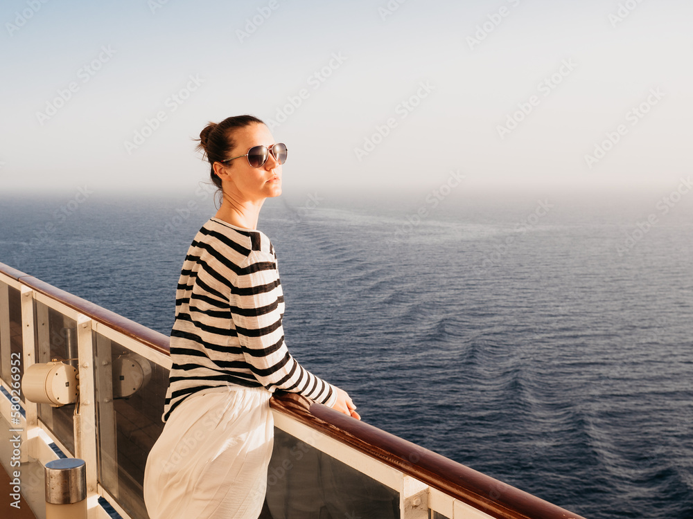 Stylish woman standing on the empty deck of a cruise ship. Sunny morning, clear day. Closeup, outdoors. Vacation and travel concept