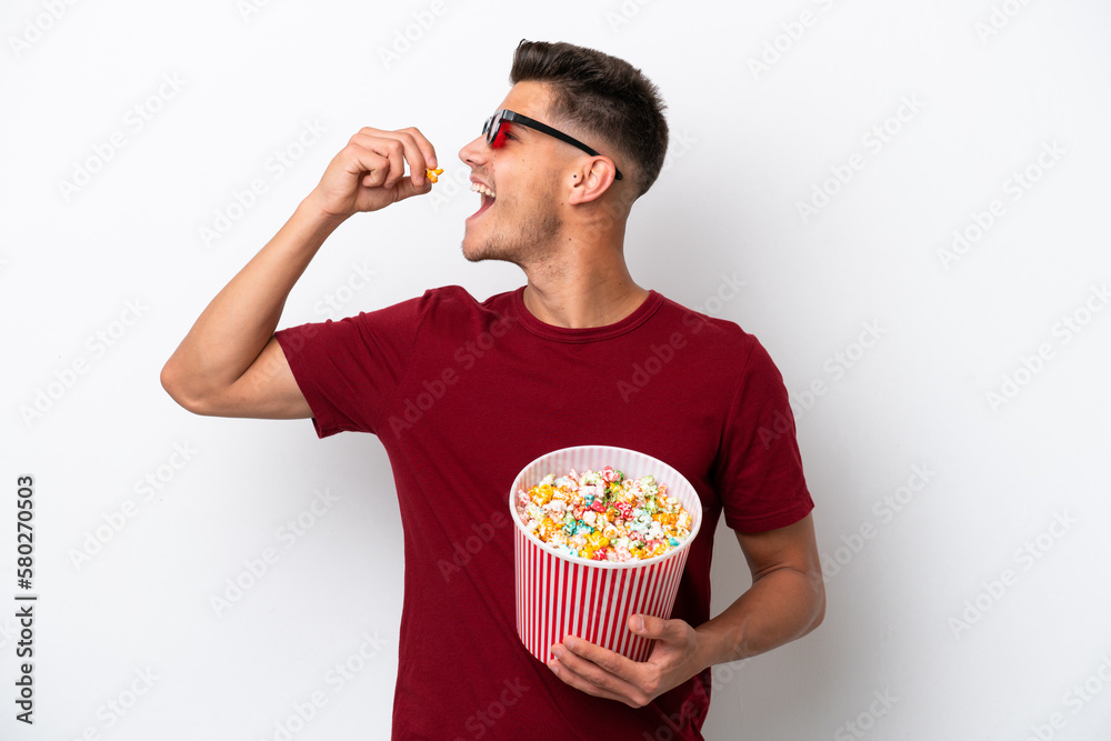 Young caucasian man isolated on white background with 3d glasses and holding a big bucket of popcorns Young caucasian man isolated on white background with 3d glasses and holding a big bucket of popcorns