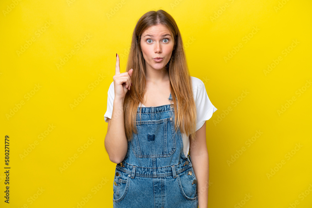 Young caucasian woman isolated on yellow background intending to realizes the solution while lifting a finger up Young caucasian woman isolated on yellow background intending to realizes the solution while lifting a finger up