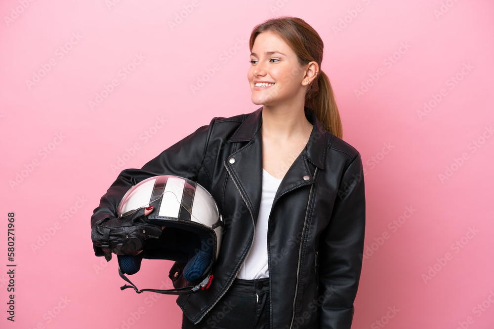 Young caucasian woman with a motorcycle helmet isolated on pink background looking to the side and smiling Young caucasian woman with a motorcycle helmet isolated on pink background looking to the side and smiling