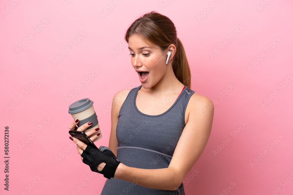 Young sport caucasian woman isolated on pink background holding coffee to take away and a mobile Young sport caucasian woman isolated on pink background holding coffee to take away and a mobile