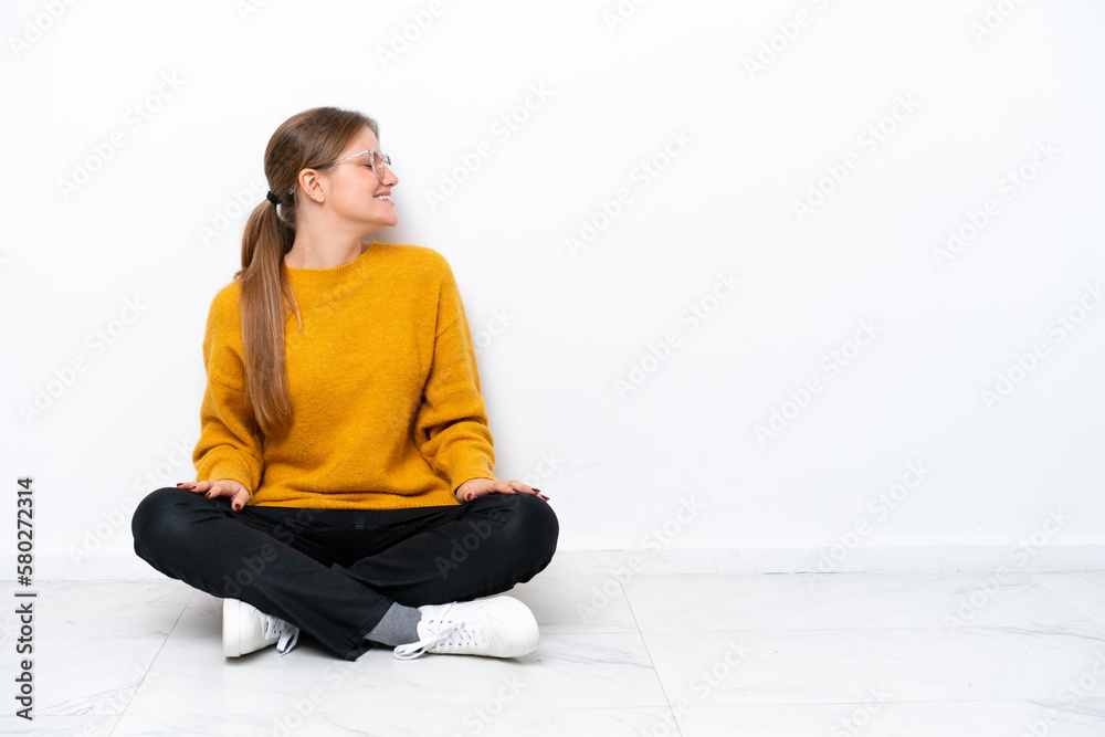 Young caucasian woman sitting on the floor isolated on white background laughing in lateral position