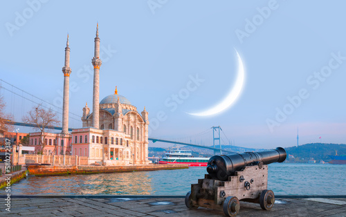 Ramadan Concept - Ortakoy mosque and Bosphorus bridge with crescent and cannon at twilight blue hour - Istanbul, Turkey © muratart