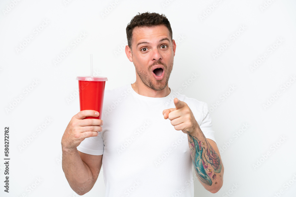 Young caucasian soda holding soda isolated on white background surprised and pointing front Young caucasian soda holding soda isolated on white background surprised and pointing front