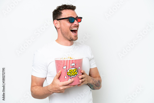 Young caucasian handsome man isolated on white background with 3d glasses and holding a big bucket of popcorns
