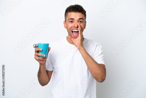 Young Brazilian man holding cup of coffee isolated on white background shouting with mouth wide open