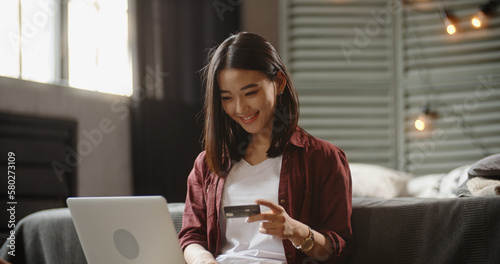 Young woman holding credit card and using laptop computer. Businesswoman or entrepreneur working at home. Online shopping, e-commerce, internet banking, spending money, working from home concept