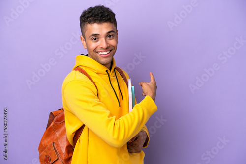 Young student Brazilian man isolated on purple background pointing back