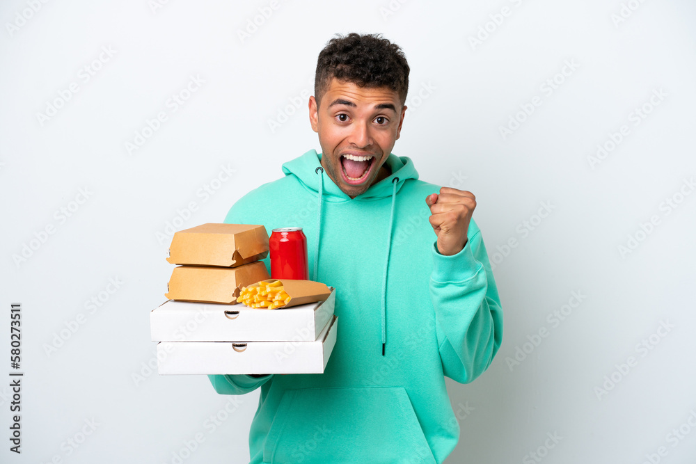 Young Brazilian holding fast food isolated on white background celebrating a victory in winner position Young Brazilian holding fast food isolated on white background celebrating a victory in winner position