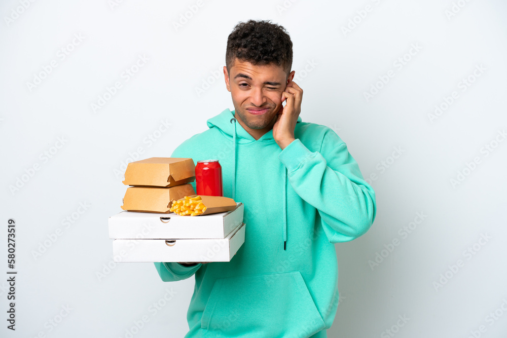Young Brazilian holding fast food isolated on white background frustrated and covering ears Young Brazilian holding fast food isolated on white background frustrated and covering ears