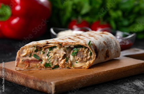 A delicious  doner kebab wrap with  meat, lettuce, tomato, onion and sauce on black background.