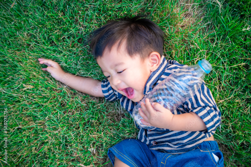 Toddler baby boy lying on green grass field holding water bottle Toddler baby boy lying on green grass field holding water bottle