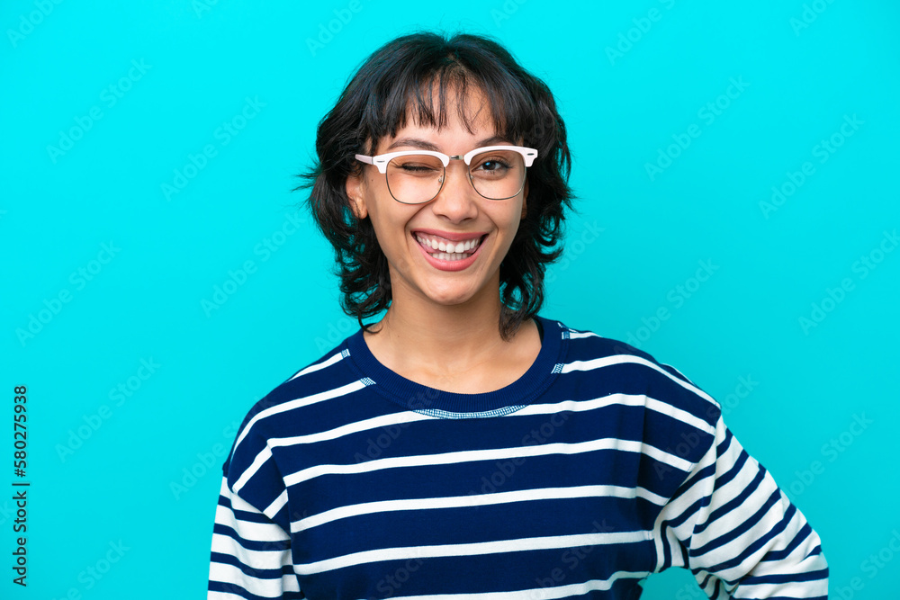 Young Argentinian woman isolated on blue background With glasses and happy expression