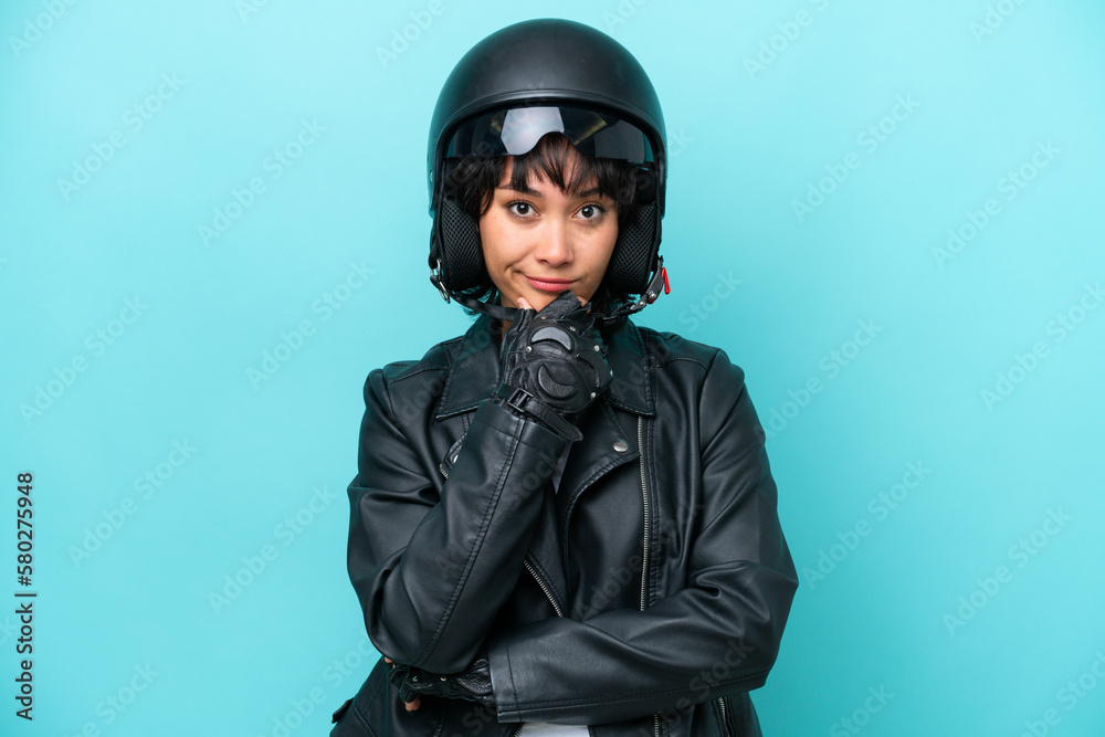 Young Argentinian woman with a motorcycle helmet isolated on blue background thinking