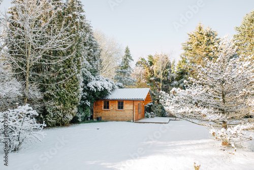 Small wooden house surrounded by many trees and snow. Winter holidays in Scandinavia, Norway or Sweden. Winter mood in the garden. Garden house for cosiness in the village