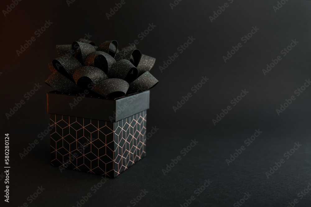 A black gift box with a geometric pattern and a black bow on a black background. Minimalist background for a holiday A black gift box with a geometric pattern and a black bow on a black background. Minimalist background for a holiday