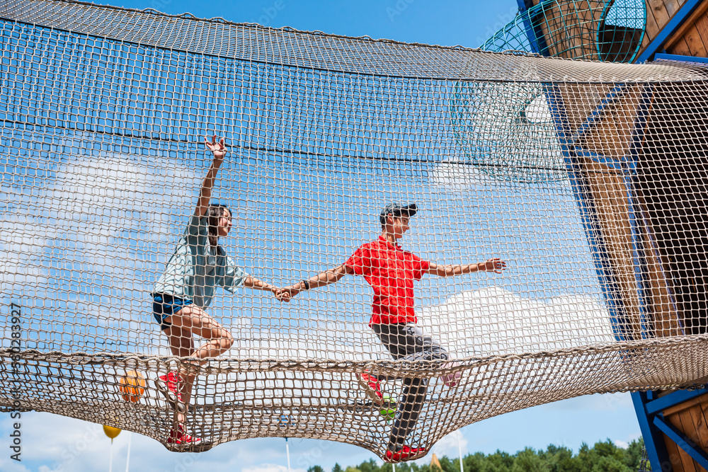 Children run and climb rope net at height in adventure amusement park.
