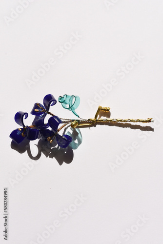 A glass flower twig, three blue flowers with golden stamens, and a blue transparent leaf, tied with a golden rope.