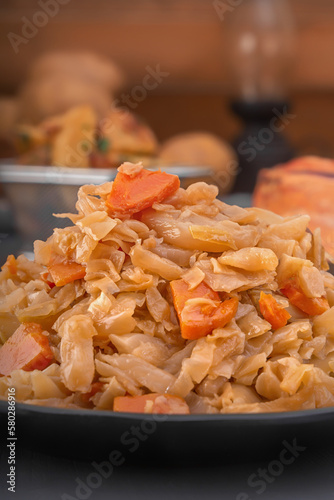 Stewed cabbage - bigos in a black plate on a dark background. Close-up photo