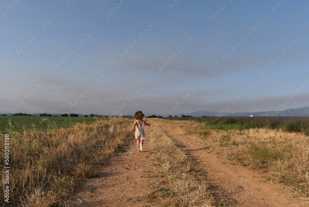 little girl enjoying the freedom of running along a path in the middle of the field.