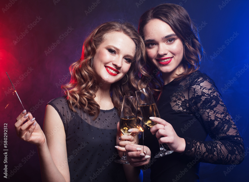 two cheerful beauty female friends holding sparklers and smile looking at the camera
