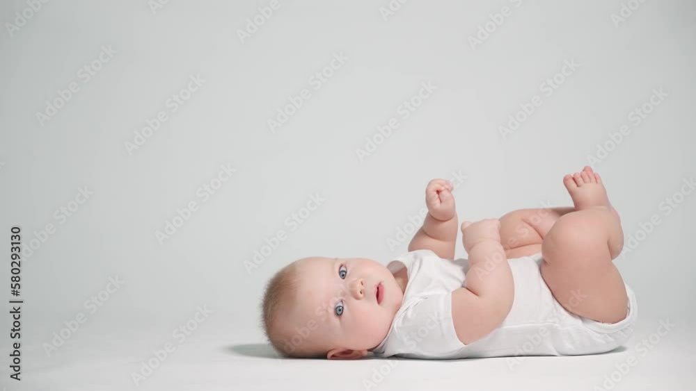 A 6-month-old baby on a white background is lying on his back looking at the cameraman. A 6-month-old baby on a white background is lying on his back looking at the cameraman.