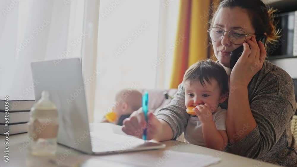 mother working from home remotely with baby daughter in his arms. pandemic remote work business a concept. mother tries to work at home in fun kitchen, baby children interfere sitting on their hands mother working from home remotely with baby daughter in his arms. pandemic remote work business a concept. mother tries to work at home in fun kitchen, baby children interfere sitting on their hands