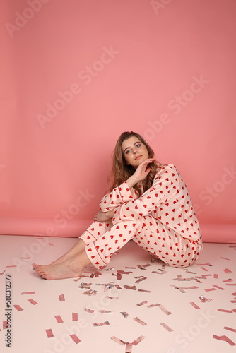 beautiful girl in heart print pajamas on a pink background. surprised look, Confetti. Pink pajamas with red hearts. clothes for sleep and home.
