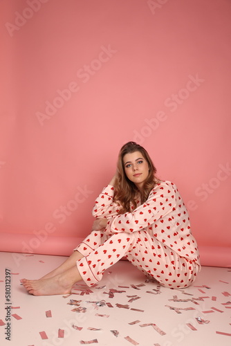 beautiful girl in heart print pajamas on a pink background. surprised look, Confetti. Pink pajamas with red hearts. clothes for sleep and home.