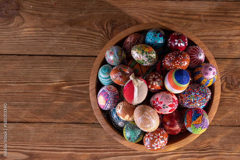 A wooden bowl with closely arranged Easter eggs stands on a background of boards. A wooden bowl with closely arranged Easter eggs stands on a background of boards.