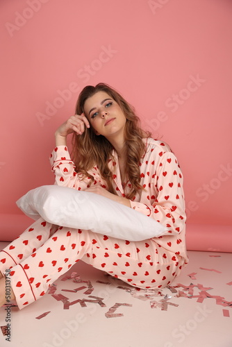 beautiful woman in heart print pajamas on a pink background with a white pillowcase. Pink pajamas with red hearts. clothes for sleep and home. Valentine's Day. beautiful blonde in pajamas lying 