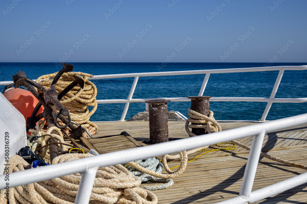 Bow of white yacht on background of blue sea.Thick anchor rope is wound around the bollards. Steel railings-fences. Top view. Close-up. Selective focus.