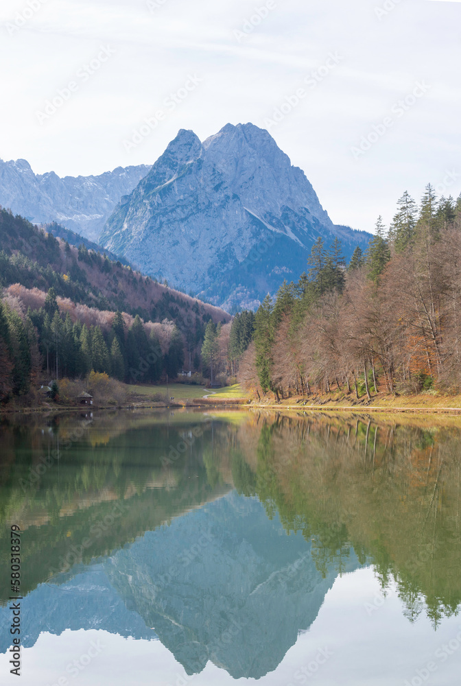 View over the Riessersee, Riessersee in the Ammergau Alps to the south to the Zugspitze in autumn. In the cold clear air the mountain panorama is well visible. The mixed forest is colored in autumn.