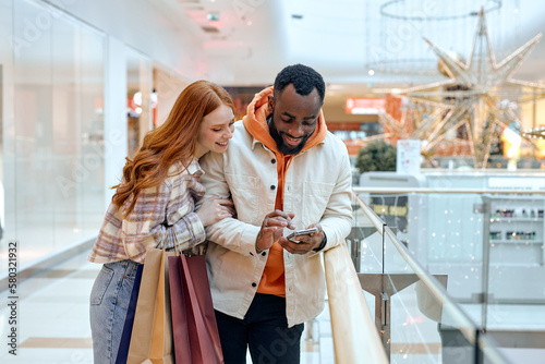 young people Using Cellphone Holding Colorful Shopper Bags Standing In Mall Happy Customers Using Application Purchasing Clothes Online Smartphone. Ecommerce Shopaholism. happiness. free spare time