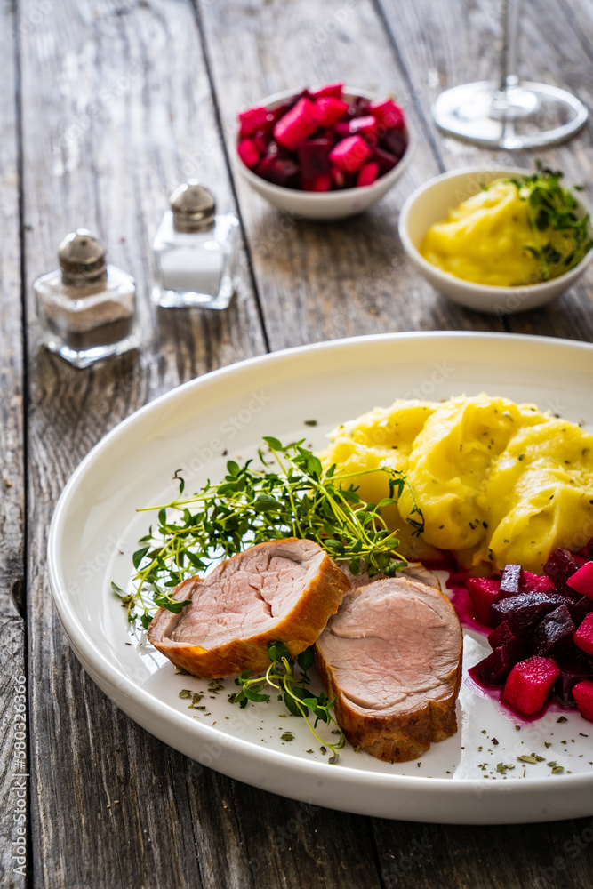 Fried pork loin with potato puree and vegetables on wooden table
