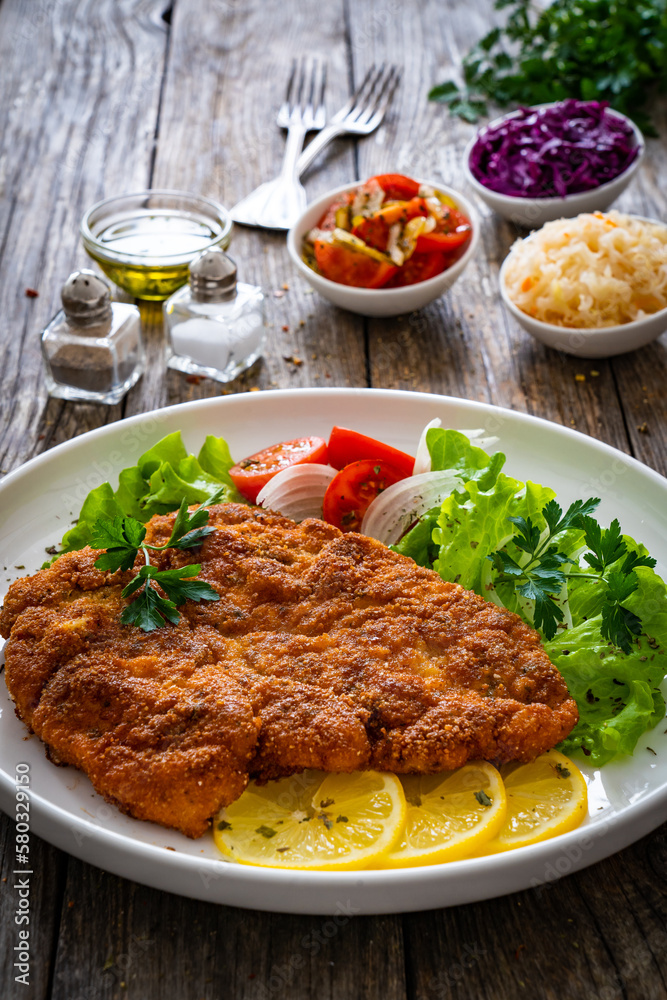 Breaded fried pork chop with cabbage salad and greens on wooden table
Breaded fried pork chop with cabbage salad and greens on wooden table