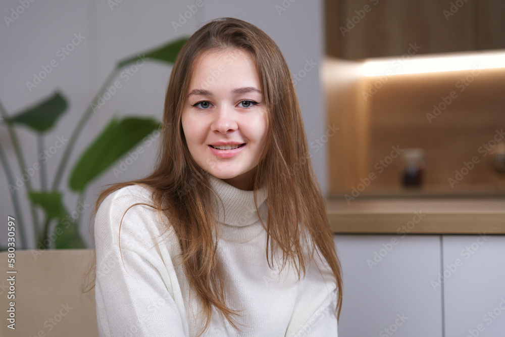 Portrait of young happy positive beautiful woman, teenager at home in living room looking at camera, smile in sweater Portrait of young happy positive beautiful woman, teenager at home in living room looking at camera, smile in sweater