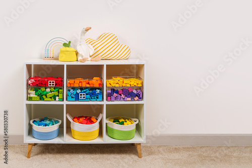 White shelving with colorful storage baskets and transparent boxes in children room. Rainbow toys in stylish baskets and plastic containers. Organizing and Storage Ideas in playroom. Interior design.