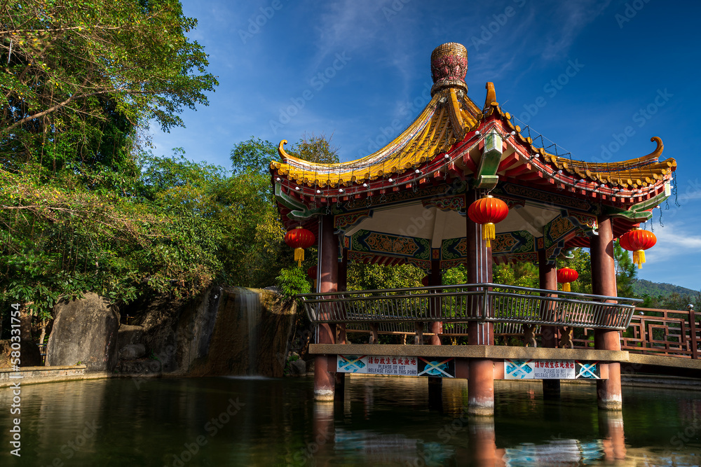 Chinese colorful gazebo on the water. Behind the gazebo there is a small waterfall and trees. Penang. Georgetown. Malaysia.
