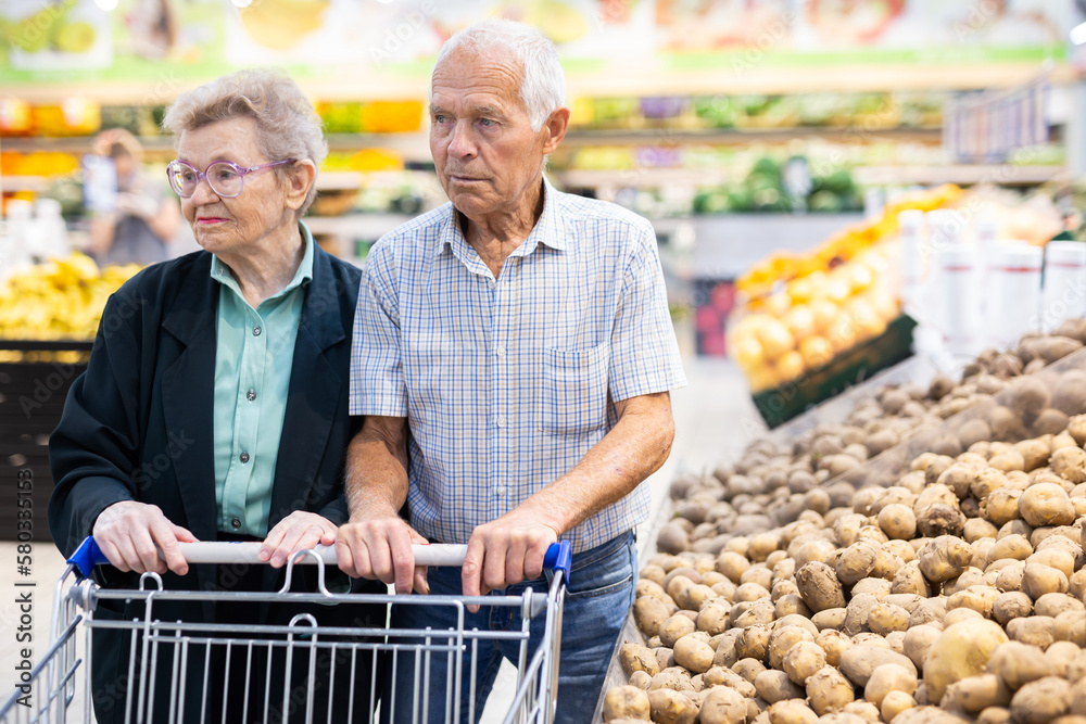 mature spouses chooses potato in vegetable section of supermarket