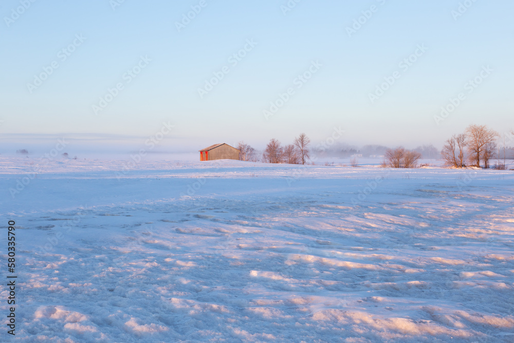 Pretty winter landscape with small wooden barn in snowy field seen at dawn, Beaumont, Bellechasse County, Quebec, Canada